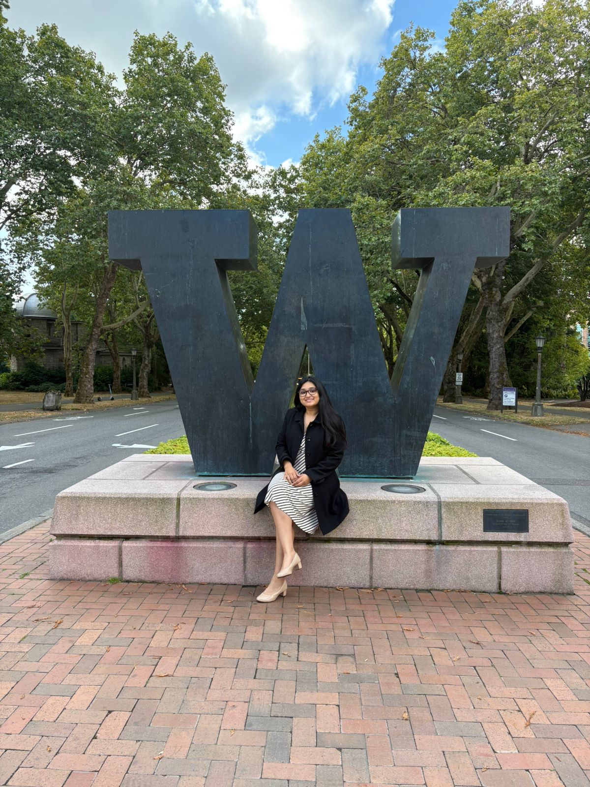 At the University of Washington campus: seated at the base of the large W statue, brick plaza and trees behind.