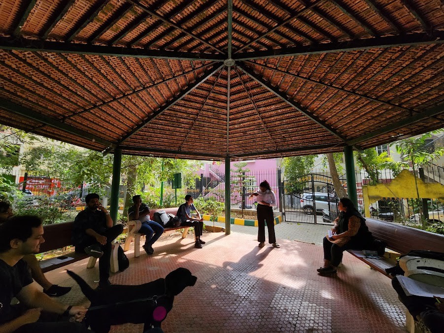 Outdoor community workshop under a gazebo: participants discussing neighbourhood routes and safety during mapping research.